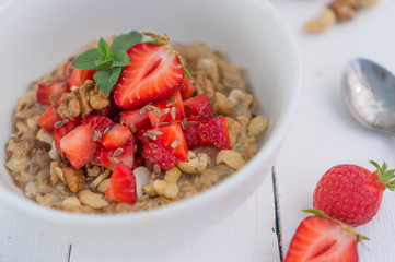 Summer healthy breakfast. Oatmeal with strawberries, walnuts, cashew nut, flax seed and mint on a white background on a wooden table. Cleansing the body. Products for weight loss. Wellness.