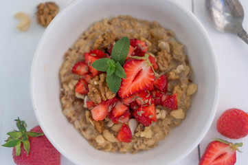 Summer healthy breakfast. Oatmeal with strawberries, walnuts, cashew nut, flax seed and mint on a white background on a wooden table. Cleansing the body. Products for weight loss. Wellness.