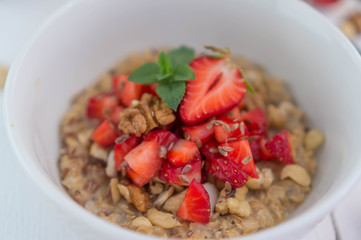 Summer healthy breakfast. Oatmeal with strawberries, walnuts, cashew nut, flax seed and mint on a white background on a wooden table. Cleansing the body. Products for weight loss. Wellness.