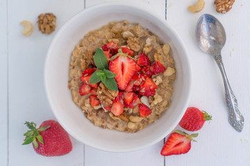 Summer healthy breakfast. Oatmeal with strawberries, walnuts, cashew nut, flax seed and mint on a white background on a wooden table. Cleansing the body. Products for weight loss. Wellness.