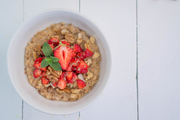 Summer healthy breakfast. Oatmeal with strawberries, walnuts, cashew nut, flax seed and mint on a white background on a wooden table. Cleansing the body. Products for weight loss. Wellness.