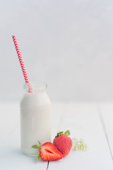 Fresh milk in a glass small bottle with a red cone, strawberry in a bowl or iron jar, cashew nuts and walnuts on a white background, on a wooden table. Morning breakfast, snacks.