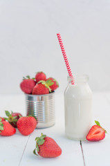Fresh milk in a glass small bottle with a red cone, strawberry in a bowl or iron jar, cashew nuts and walnuts on a white background, on a wooden table. Morning breakfast, snacks.