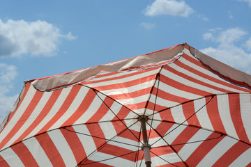 Red striped umbrella parasol to provide shade and sun protection against blue sky with light clouds