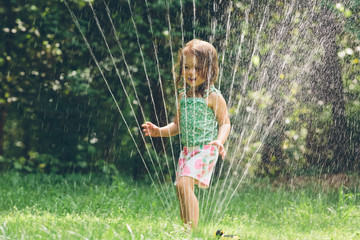 Happy toddler girl playing in a sprinkler - obrazy, fototapety, plakaty