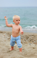 Blond baby standing on the beach on a cloudy day