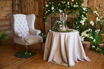 spring arbor, overgrown with greenery. A cozy corner with a soft arm-chair, a table, candles. Rustic style. Wooden interior with greenery