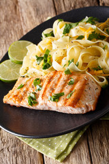 Pasta fetuccini with cheddar and grilled salmon on a plate close-up. vertical