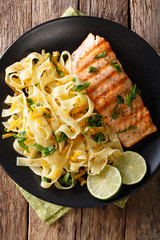 Pasta fetuccini with cheese cheddar and grilled salmon with herbs on a plate close-up. vertical top view