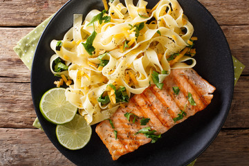 Pasta fetuccini with cheese cheddar and grilled salmon with herbs on a plate close-up. Horizontal...