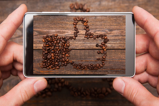 Social network. Mobile food photography. Thumbs up made by coffee beans. Popular shape for communication and advertisement on wooden background , top view