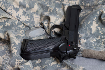 Army badge and black pistol on the background of camouflage