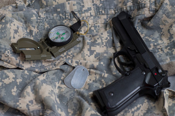 Army badge, pistol and compass on the background of camouflage