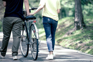 Obraz premium Back view of young couple walking together with bicycle in the garden in vintage color tone