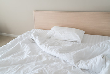 Empty bed with disheveled pillow and sheets - pillows and crumpled sheets, white linen cloth with copy space
