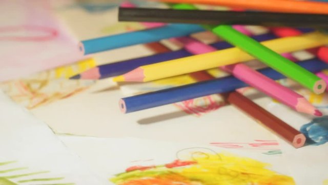 Color pencils are folded on children's drawings and rotate. Shallow depth of field