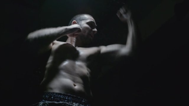 Low angle shot of shirtless muscular sportsman shadow fighting and training his punches in darkness 