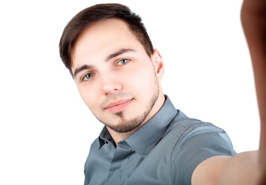 Handsome man making selfie and smiling. Picture of young cheerful man over white background standing while make a selfie by camera.