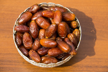 Dates fruit on a silver bowl on wooden table. The Muslim feast of the holy month of Ramadan Kareem