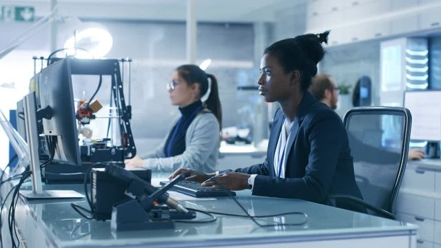 Black Female Scientist Working on a Computer with Her Colleagues at Research Center. Her Coworkers are Man and Female Caucasian. Laboratory is Modern. Shot on RED EPIC-W 8K Helium Cinema Camera.