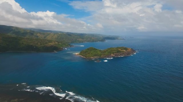 The coast of the tropical island with the mountains and the rainforest on a background of ocean with big waves.Aerial view: sea and the tropical island with rocks, beach and waves. Seascape: sky