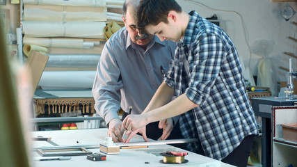 Young trainee trying to cut a glass for the frame, seniour worker watching