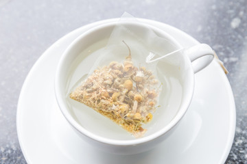 Top view of aroma chamomile tea bag floating on white teacup, ready to served in afternoon tea.