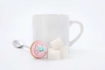 White cup with cubes of sugar and a spoon with a cake on a white background