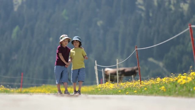 Happy children walking on a rural path in Swiss Alps, springtime, cows in the field