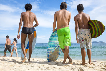 Young Brazilian men stand with skimboard on the shore of Ipanema Beach in Rio de Janeiro, Brazil