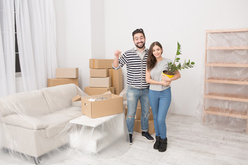 Fototapeta na wymiar Young couple moving to new apartment. Happily smiling man and woman just moved to a new home. Man keeping keys in one hand and woman keeping indoor plant.
