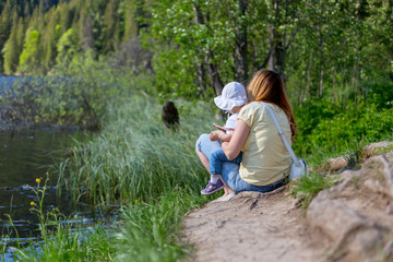 Mother and daughter sitting on the shore of a lake during summer