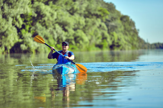  Man paddling a kayak on summer day.