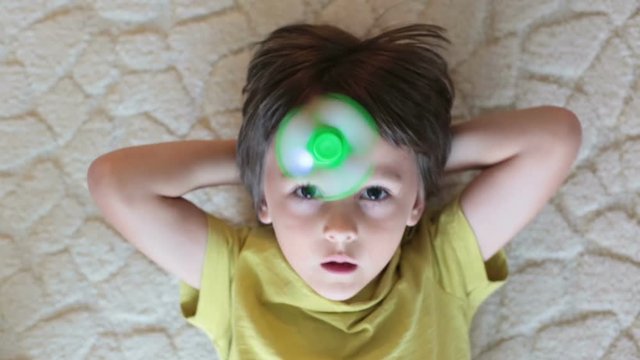 Little child, boy, playing with green and blue luminous fidget spinner toy to relieve stress at home