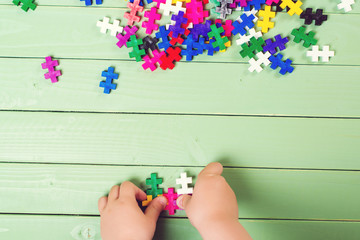 A lot of puzzles on wooden table. Child connects puzzles.