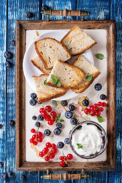 Variety of ingredients for making dessert sandwiches with bread, berries, cream cheese. Red currant, blueberries, sliced kiwi, figs over blue wood plank background. Flat lay, summer appetizer concept