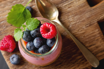 Fresh homemade yogurt in a glass jar with blueberries, raspberries, mint and Passionfruit. On a wooden board, metal vintage spoon. Dark background. Top view