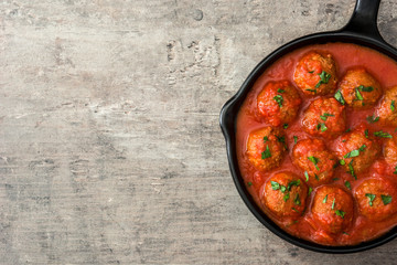 Meatballs with tomato sauce in iron frying pan on wooden table. Top view