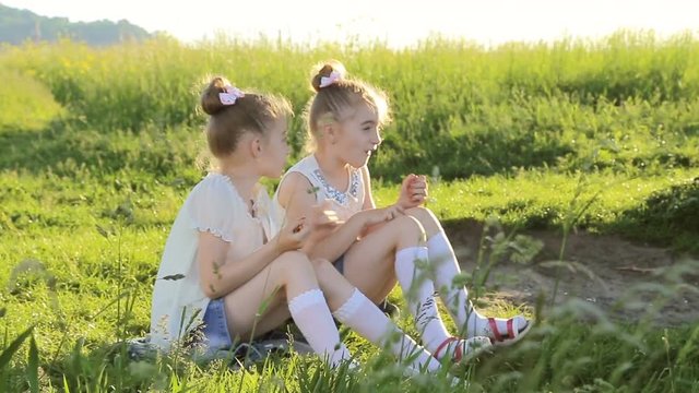 Two little girls sitting on grass talking have fun