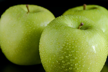 Green apples with droplets on black background