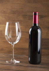 Red wine bottle and a glass placed on wooden table. Copy space. Vertical studio shot