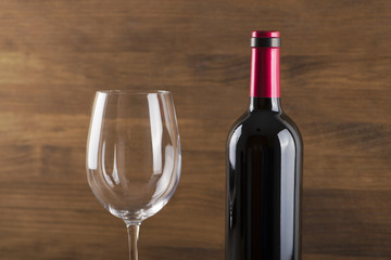Close-up of red wine bottle and a glass placed on wooden table. Copy space. Horizontal studio shot