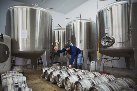 Man standing next to a row of metal beer kegs, filling them with beer from the fermentation tanks.