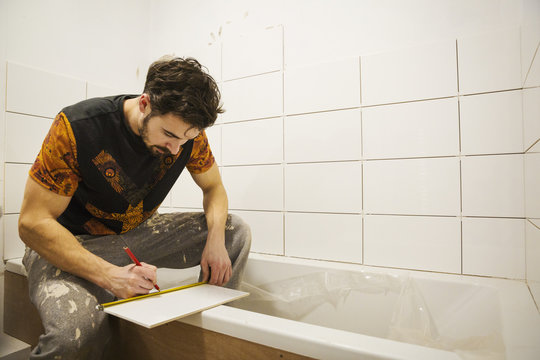 A builder, tiler working in a bathroom, marking a tile with a pencil.