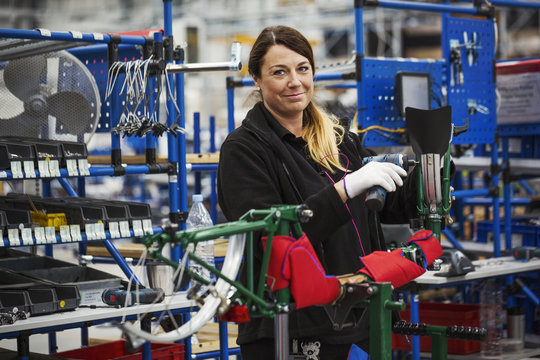Female skilled factory worker assembling bicycle in factory working on frame and wheels
