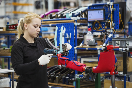Female skilled factory worker assembling a bicycle handling the brakes assembly and part of the frame. 