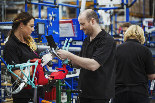 Three cycle factory workers, two women and a man assembling a bicycle in a factory.
