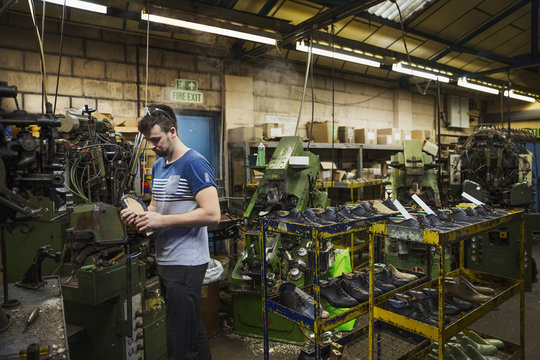 Man standing in a shoemaker's workshop by a machine and holding a cycling shoe. 