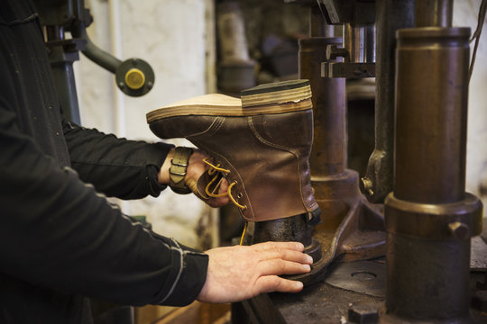 Close up of worker in a shoemaker's workshop, using a machine to make a leather ankle boot.