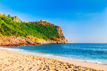 Fototapeta na wymiar Cleopatra beach on sea coast with green rocks in Alanya peninsula, Antalya district, Turkey. Beautiful sunny landscape for tourism with clear water and sand. Alanya Castle on the cliff